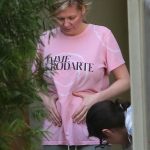 Kirsten Dunst holding her pregnant stomach in a pink t shirt