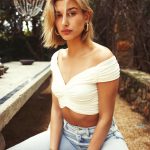 Hailey Baldwin sitting with her legs spread in jeans and a white crop top